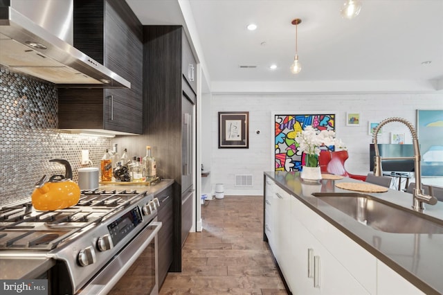 kitchen featuring sink, wall chimney range hood, decorative light fixtures, high end stainless steel range, and white cabinets