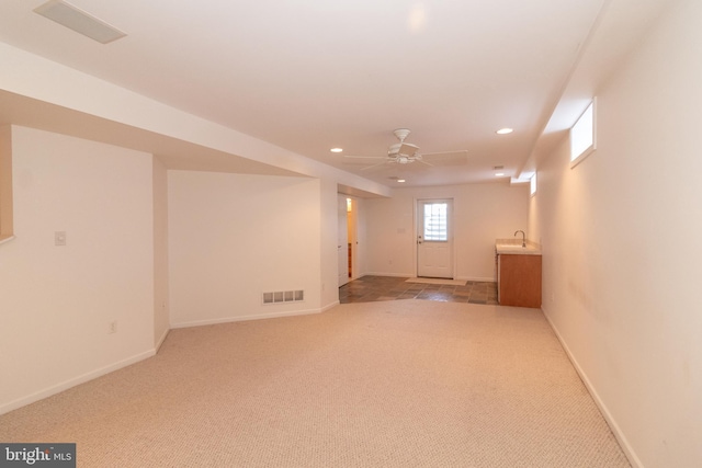 basement featuring ceiling fan, sink, and light carpet