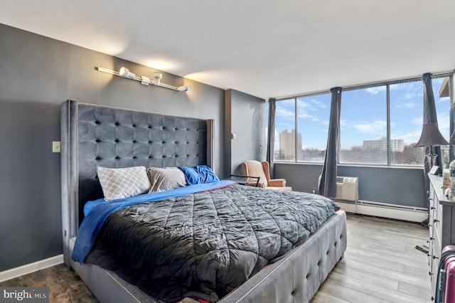 bedroom featuring a wall mounted AC, hardwood / wood-style floors, and baseboard heating