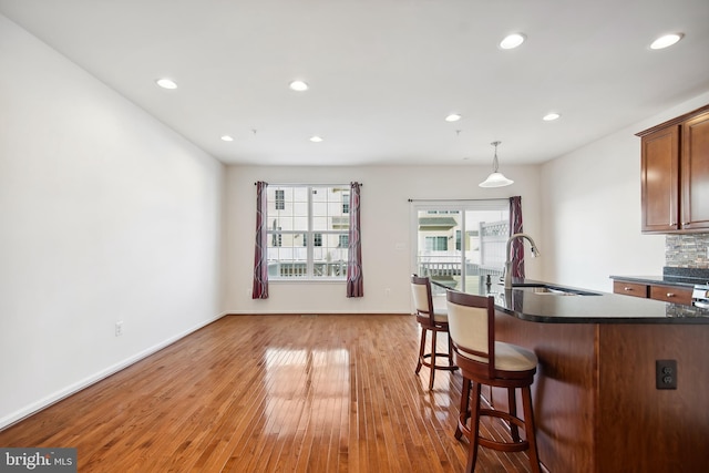 kitchen with backsplash, sink, light wood-type flooring, decorative light fixtures, and a breakfast bar area