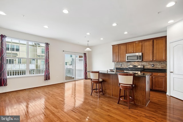 kitchen featuring a kitchen breakfast bar, stainless steel appliances, decorative light fixtures, hardwood / wood-style floors, and an island with sink