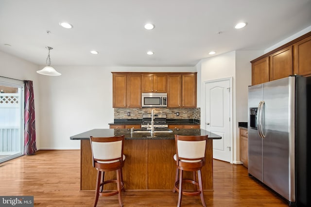 kitchen featuring decorative light fixtures, stainless steel appliances, light hardwood / wood-style flooring, and a kitchen island with sink