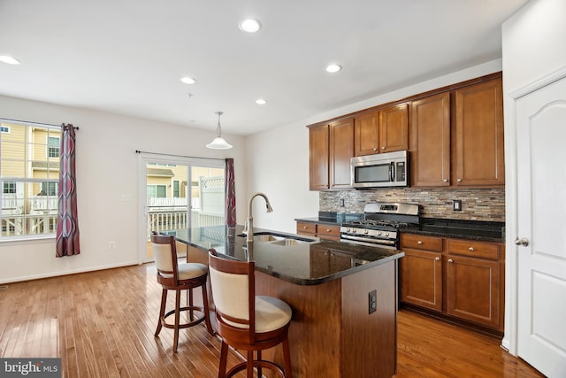 kitchen with sink, decorative light fixtures, decorative backsplash, a center island with sink, and appliances with stainless steel finishes