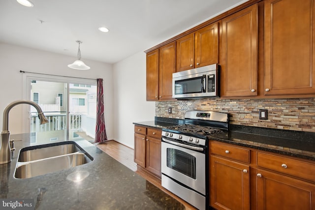 kitchen featuring sink, stainless steel appliances, tasteful backsplash, dark stone countertops, and pendant lighting