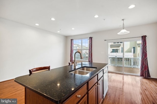 kitchen with dark stone counters, sink, light hardwood / wood-style flooring, an island with sink, and decorative light fixtures