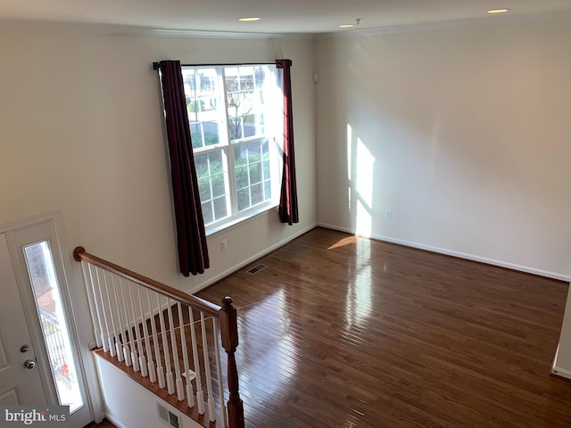 empty room featuring a healthy amount of sunlight, crown molding, and dark wood-type flooring