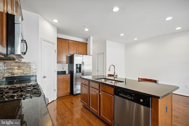 kitchen featuring dark stone counters, stainless steel appliances, dark wood-type flooring, sink, and a center island with sink