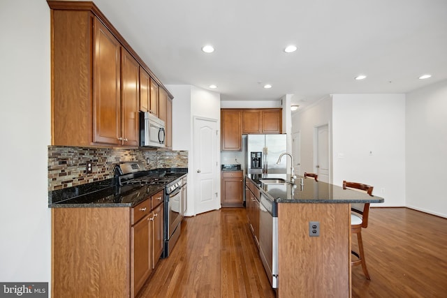 kitchen with dark stone counters, sink, an island with sink, wood-type flooring, and stainless steel appliances