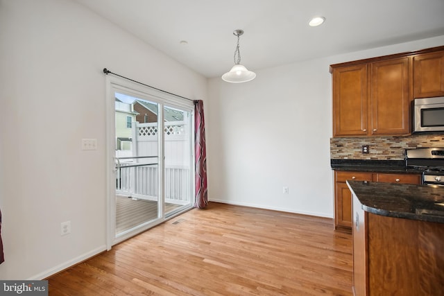 kitchen featuring decorative backsplash, appliances with stainless steel finishes, dark stone counters, pendant lighting, and light hardwood / wood-style floors