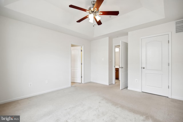 unfurnished bedroom with ceiling fan, light carpet, and a tray ceiling