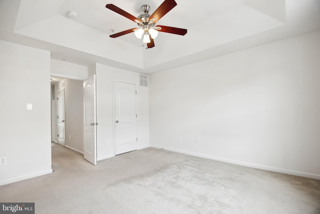 unfurnished bedroom featuring a raised ceiling, ceiling fan, and light colored carpet