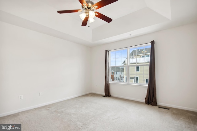 empty room with a tray ceiling, ceiling fan, and light colored carpet