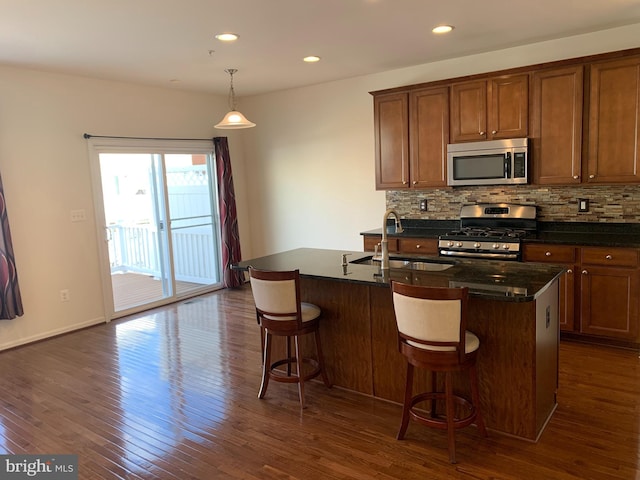 kitchen with stainless steel appliances, sink, decorative light fixtures, a center island with sink, and dark hardwood / wood-style floors