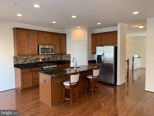 kitchen featuring appliances with stainless steel finishes, a breakfast bar, a kitchen island with sink, sink, and dark stone countertops