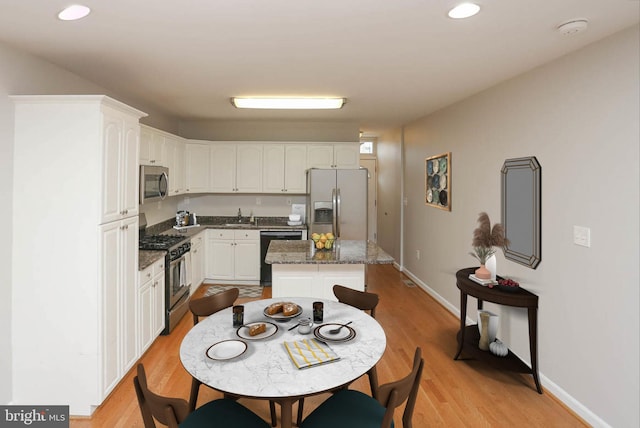 kitchen featuring a center island, appliances with stainless steel finishes, dark stone counters, white cabinets, and light wood-type flooring