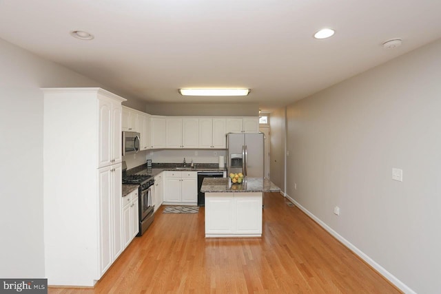 kitchen with dark stone counters, light wood-type flooring, appliances with stainless steel finishes, a kitchen island, and white cabinetry