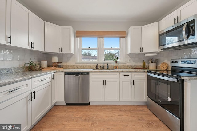 kitchen featuring sink, decorative backsplash, appliances with stainless steel finishes, light hardwood / wood-style floors, and white cabinetry