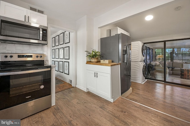 kitchen with hardwood / wood-style flooring, white cabinetry, stacked washer / dryer, and appliances with stainless steel finishes