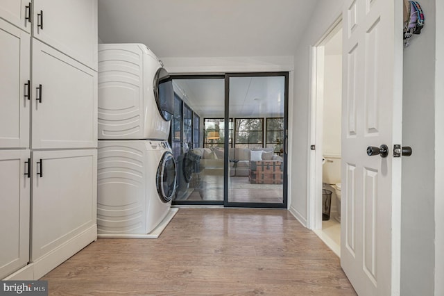 laundry area with cabinets, light hardwood / wood-style flooring, and stacked washing maching and dryer