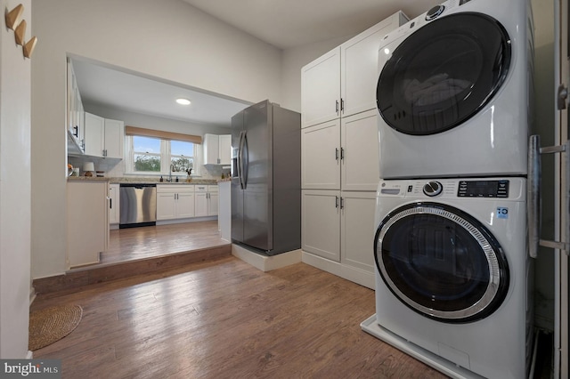 laundry area with cabinets, wood-type flooring, stacked washer / dryer, and sink