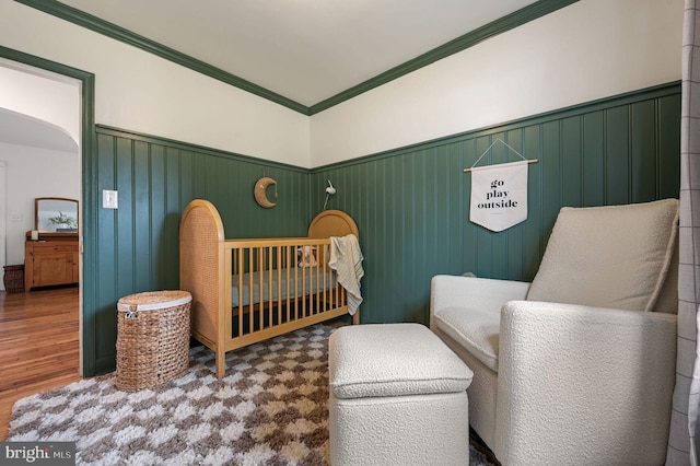 bedroom featuring wood-type flooring, a crib, and ornamental molding