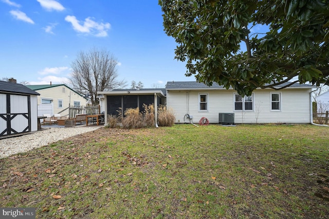 rear view of property with a sunroom, a storage unit, central air condition unit, and a yard