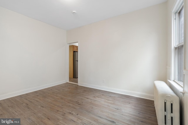 unfurnished room featuring hardwood / wood-style floors, radiator, and a healthy amount of sunlight