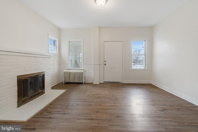 unfurnished living room with radiator heating unit, dark hardwood / wood-style floors, and a brick fireplace