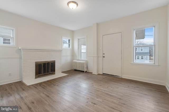 unfurnished living room featuring radiator heating unit, light hardwood / wood-style flooring, and a brick fireplace