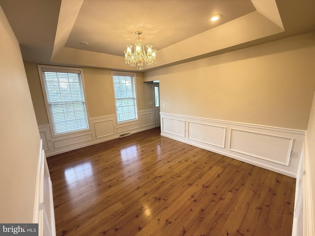 unfurnished room featuring a raised ceiling, dark hardwood / wood-style floors, and an inviting chandelier