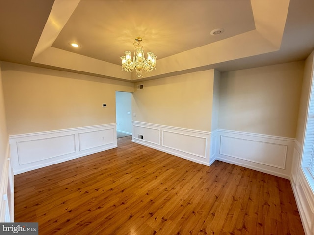 unfurnished room with wood-type flooring, a tray ceiling, and an inviting chandelier