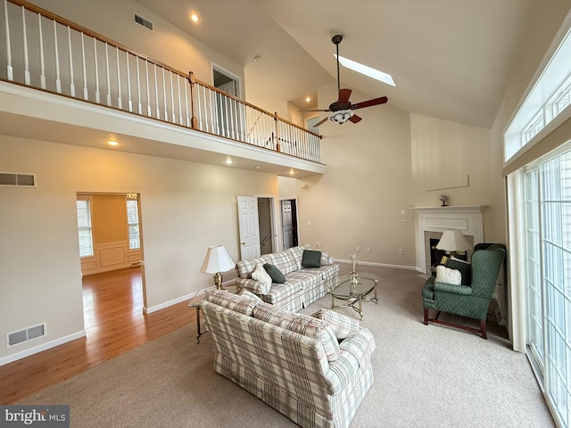 carpeted living room featuring ceiling fan, a healthy amount of sunlight, high vaulted ceiling, and a skylight