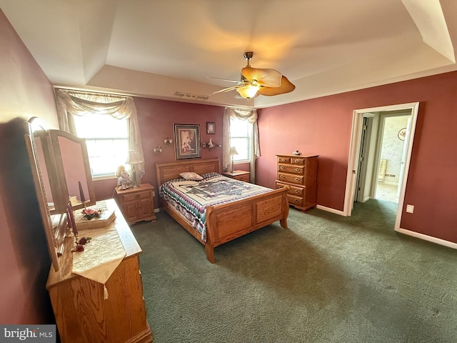 bedroom with a raised ceiling, ceiling fan, ensuite bathroom, and dark colored carpet