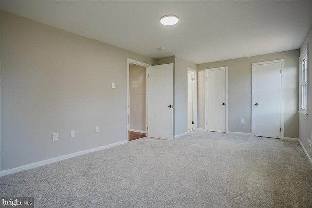 unfurnished bedroom featuring light colored carpet and multiple closets