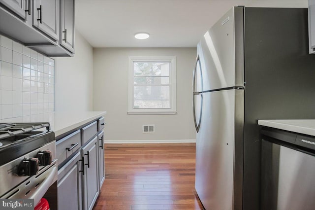 kitchen with backsplash, gray cabinets, stainless steel appliances, and light wood-type flooring