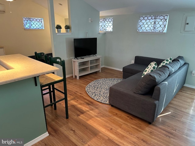 living room featuring lofted ceiling, wood-type flooring, electric panel, and an AC wall unit