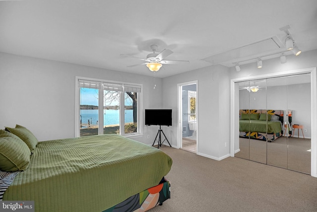 carpeted bedroom featuring rail lighting, connected bathroom, ceiling fan, and a closet