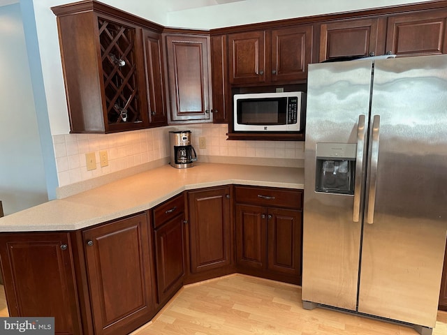 kitchen with tasteful backsplash, light wood-type flooring, kitchen peninsula, and appliances with stainless steel finishes