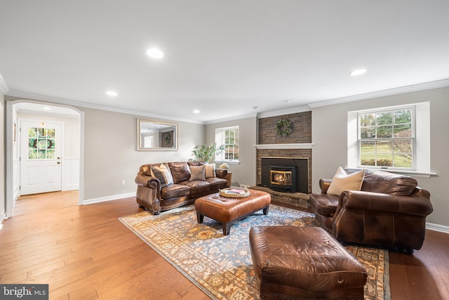 living room with a stone fireplace, ornamental molding, and light hardwood / wood-style flooring