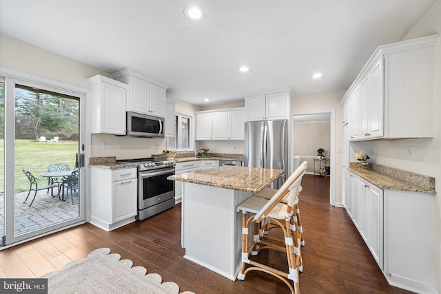 kitchen with dark hardwood / wood-style floors, appliances with stainless steel finishes, a kitchen island, light stone counters, and white cabinetry