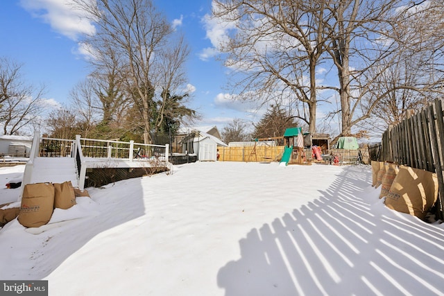 yard layered in snow with a playground, a deck, and a storage shed