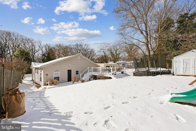 snow covered rear of property with a trampoline, a deck, and a storage unit