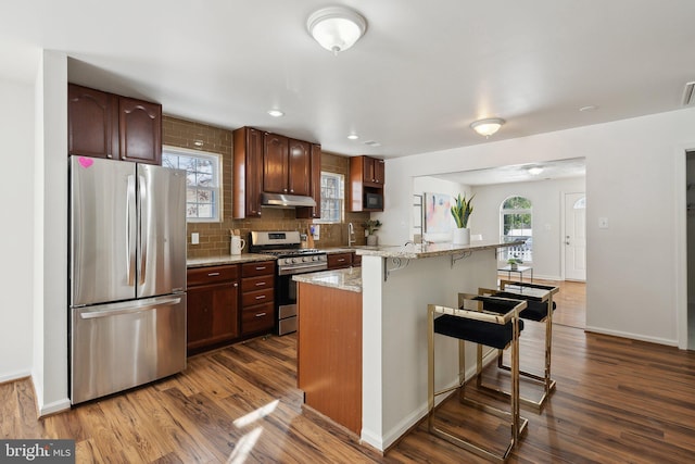 kitchen featuring light stone countertops, a wealth of natural light, a breakfast bar, stainless steel appliances, and dark hardwood / wood-style floors