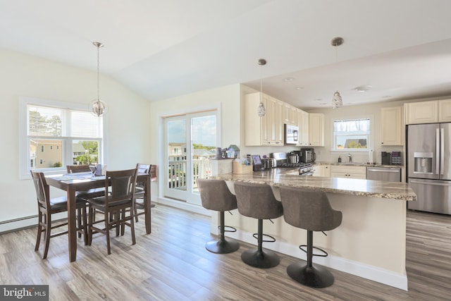 kitchen with kitchen peninsula, appliances with stainless steel finishes, light stone countertops, a breakfast bar, and pendant lighting