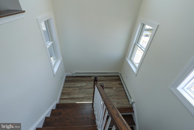 staircase with plenty of natural light, a baseboard radiator, and wood-type flooring