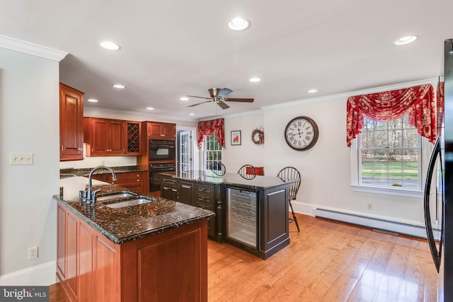 kitchen featuring sink, baseboard heating, double oven, dark stone counters, and a kitchen island with sink