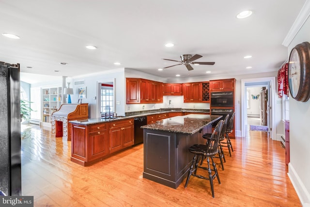 kitchen with a center island, dark stone counters, a breakfast bar, black appliances, and light wood-type flooring