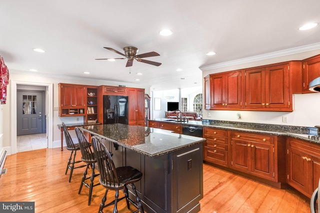 kitchen featuring a kitchen bar, ceiling fan, black appliances, dark stone countertops, and a center island