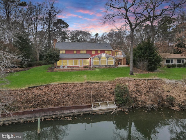 back house at dusk with a yard and a water view