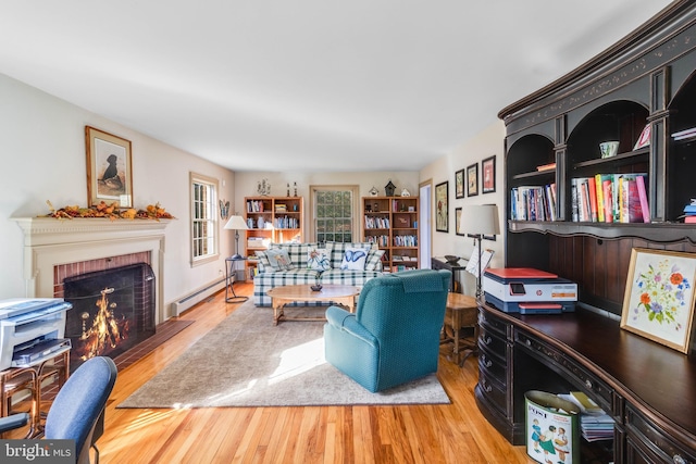 living room with light hardwood / wood-style floors, baseboard heating, and a brick fireplace